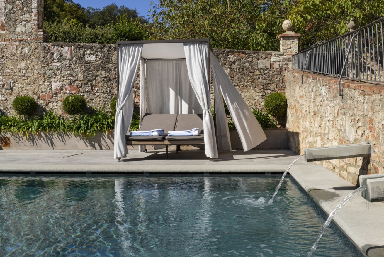 Un área junto a la piscina con una cama con dosel, pared de piedra y una pequeña piscina.