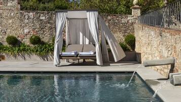 Un área junto a la piscina con una cama con dosel, pared de piedra y una pequeña piscina.
