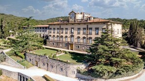 Un edificio grande e histórico con un patio central, rodeado de árboles y un muro de piedra.