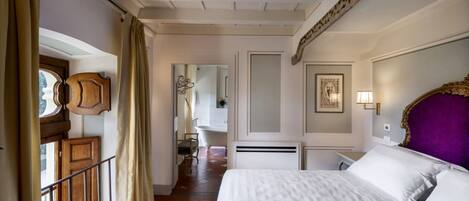 A hotel room with a large bed, a wooden headboard, a bathroom with a bathtub, and a balcony with a railing.