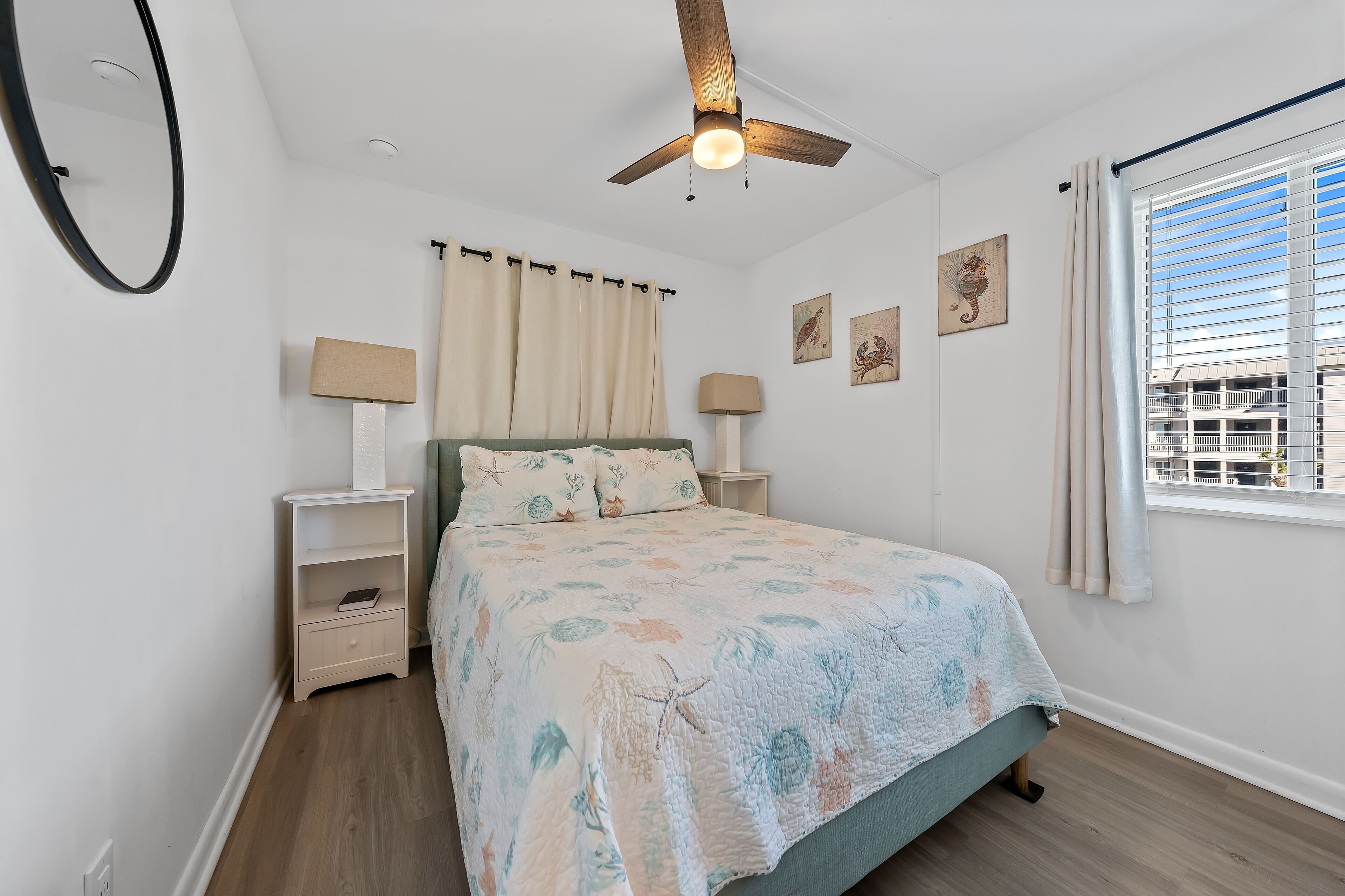 A bedroom with a bed, nightstands, a ceiling fan, curtains, and wall art.