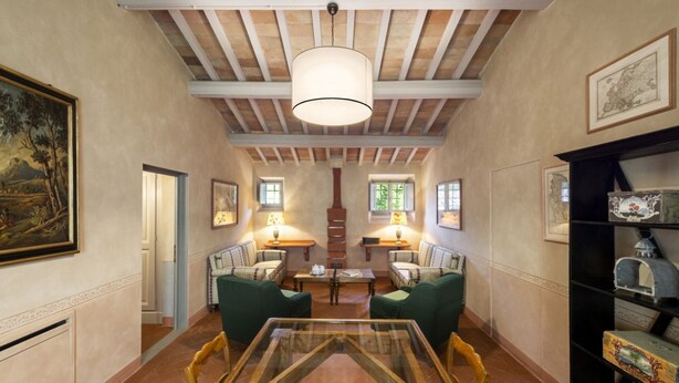A spacious room with a high ceiling, wooden beams, a glass table, green chairs, and a fireplace. - My Exclusive Italy - Classic Suite in a Luxury Wine Estate (Rignano sull'Arno)