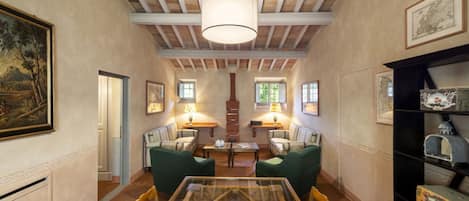 Una habitación amplia con techo alto, vigas de madera, una mesa de vidrio, sillas verdes y una chimenea.