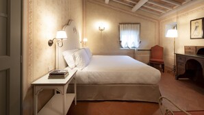 Een hotelkamer met een bed, nachtkastje, lamp, stoel, bureau en een open haard.