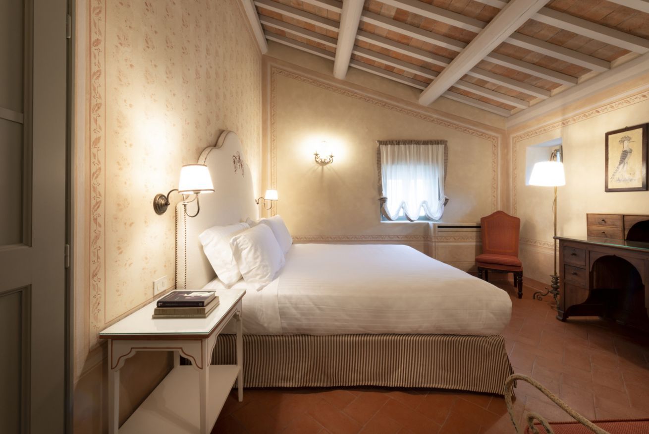 A hotel room with a bed, bedside table, lamp, chair, desk, and a fireplace.