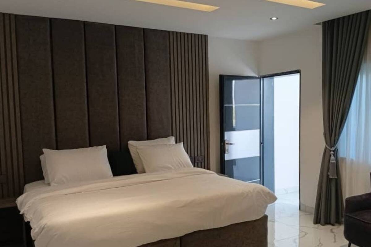 Quarto de hotel moderno com uma cama grande, uma cadeira e vista para o exterior.
