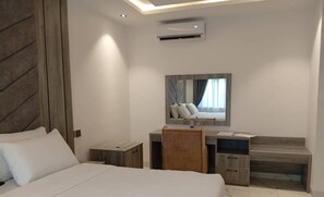A modern hotel room with a large bed, a desk with a chair, a vanity, and a mirror. - CALICO HOTEL & SUITES ABUJA (Abuja)