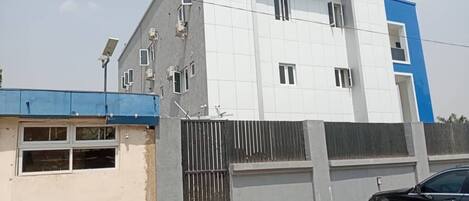 Un edificio moderno con fachada blanca y azul, una entrada protegida por una reja y paneles solares en el techo.