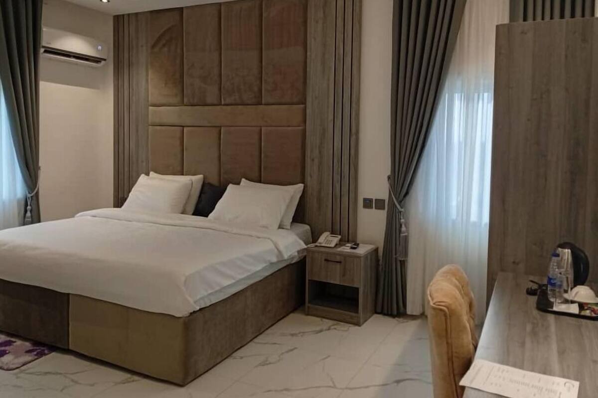 Quarto de hotel moderno com uma cama grande, uma mesinha de cabeceira com telefone e uma escrivaninha com cadeira.