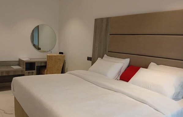 A hotel room with a large bed, a bedside table, a round mirror, and a wooden headboard. - CALICO HOTEL & SUITES ABUJA (Abuja)