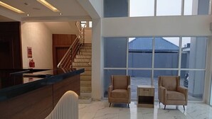 Un vestíbulo amplio con un mostrador de recepción, dos sillones, una mesita y una escalera que conduce a un nivel superior.