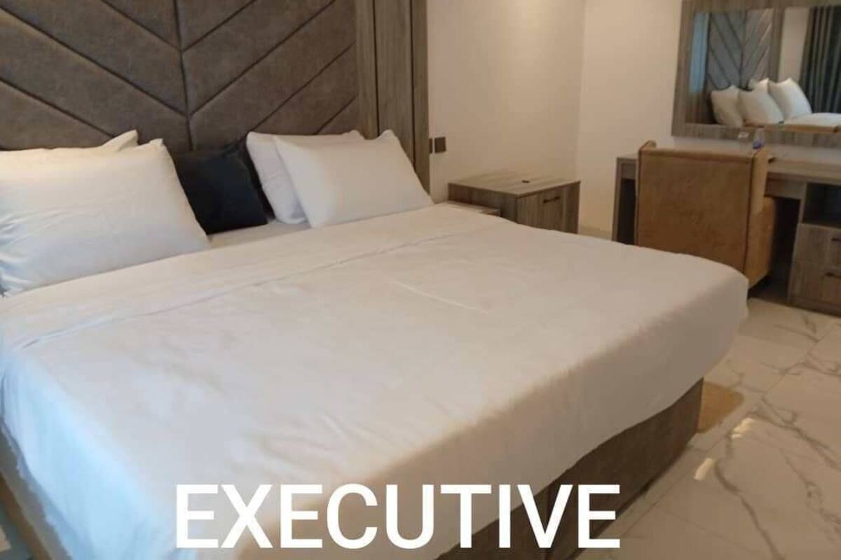 Um quarto executivo espaçoso, com uma cama grande, cabeceira de madeira, mesa de cabeceira e toucador com espelho.