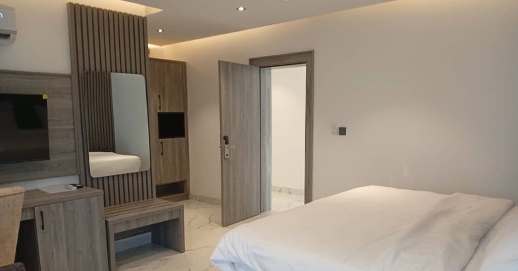 Un dormitorio moderno con una cama, un tocador con espejo y una puerta que da a otra habitación.