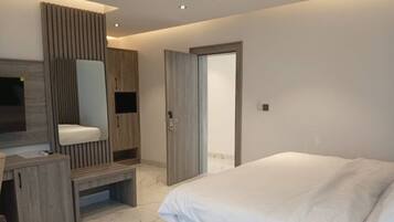 Un dormitorio moderno con una cama, un tocador con espejo y una puerta que da a otra habitación.