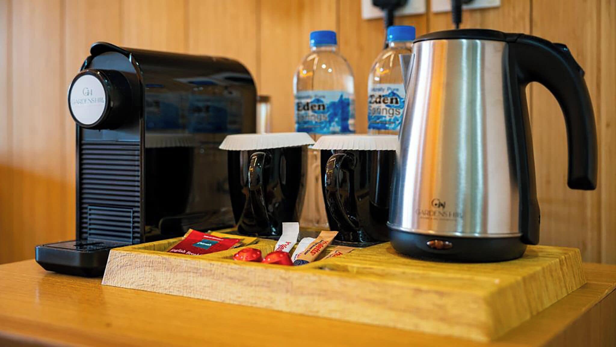 Una cocina con cafetera, dos botellas de agua, hervidor y tabla de cortar con alimentos.
