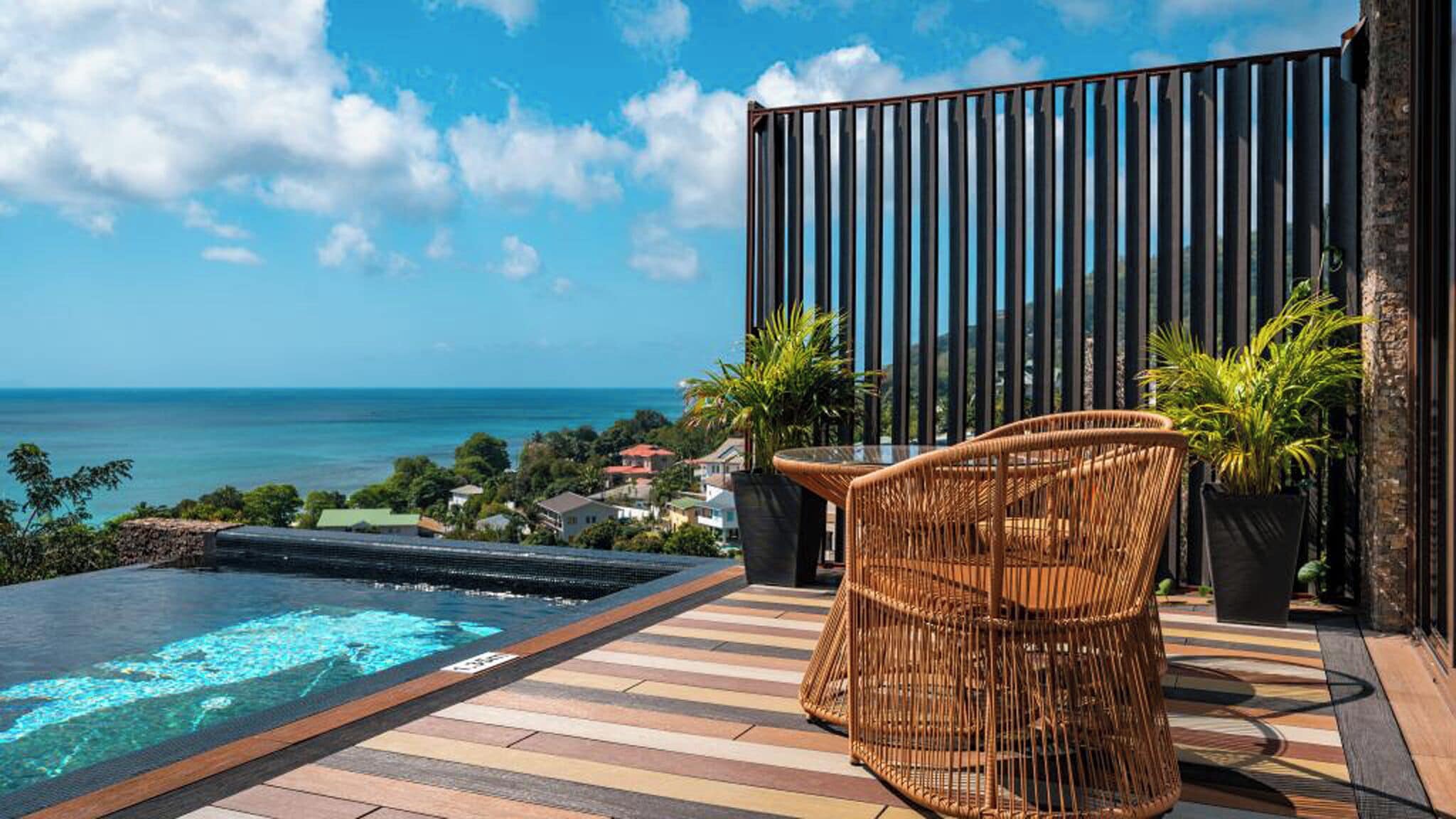 A balcony with a view of the ocean, a hot tub, and wicker furniture.