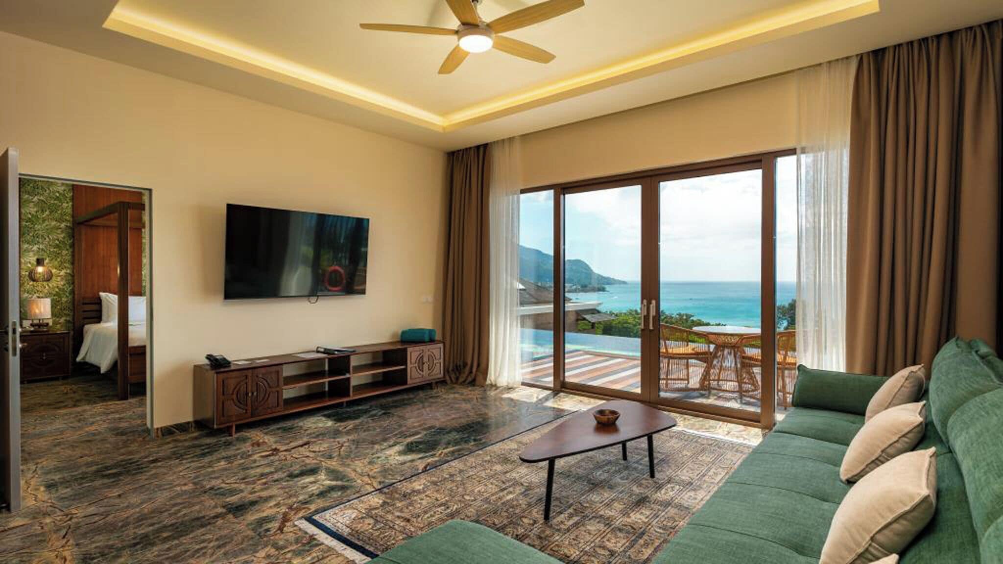 A modern living room with a flat-screen TV, a sofa, a coffee table, and a view of the ocean.