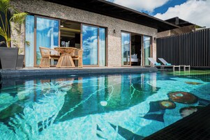 A modern pool area with a glass-enclosed patio, lounge chairs, and a dining set.