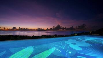 An infinity pool with a water feature at dusk.