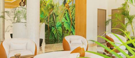 Un hall con dos sillones blancos, una mesa de centro de madera y un mural con una escena de selva.