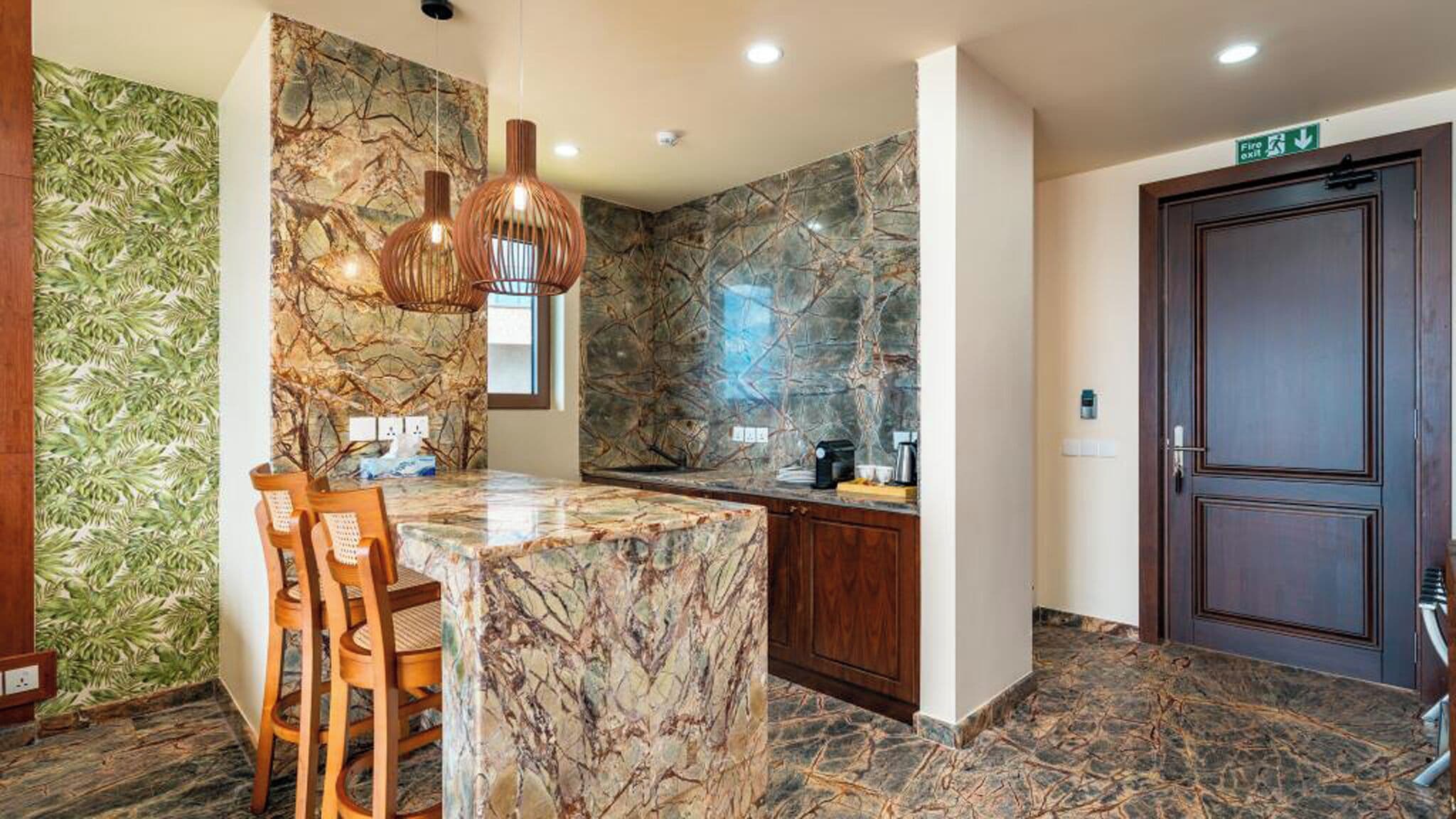 Una cocina moderna con una isla de mármol, sillas de madera, luces colgantes y una pared de piedra.