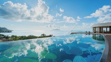 Una piscina infinita con vista al océano y una isla distante, rodeada por un edificio moderno con una terraza cubierta.