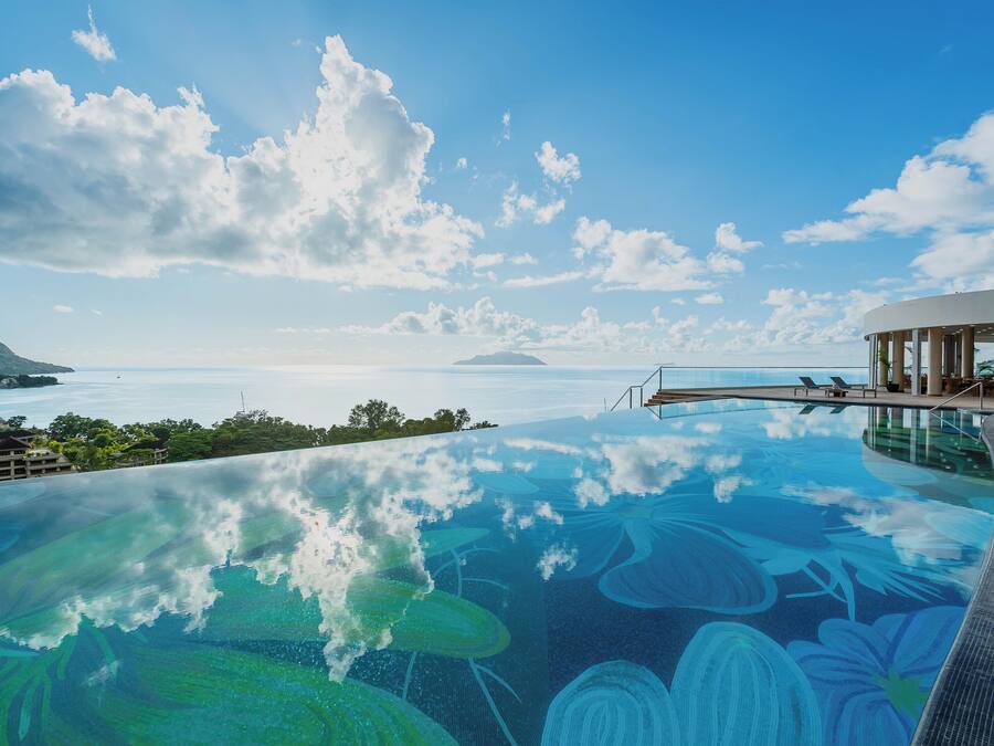 Una piscina infinita con vista al océano y una isla distante, rodeada por un edificio moderno con una terraza cubierta.