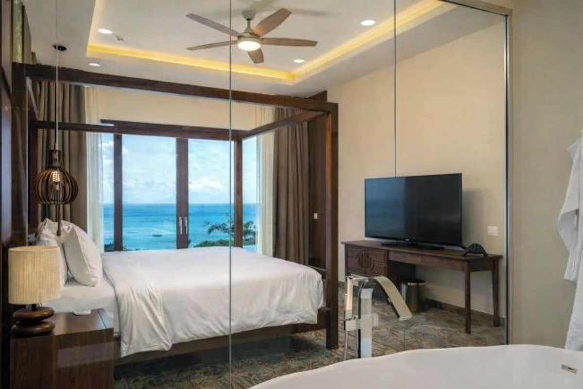 A hotel room with a bed, a television, a desk, and a view of the ocean.