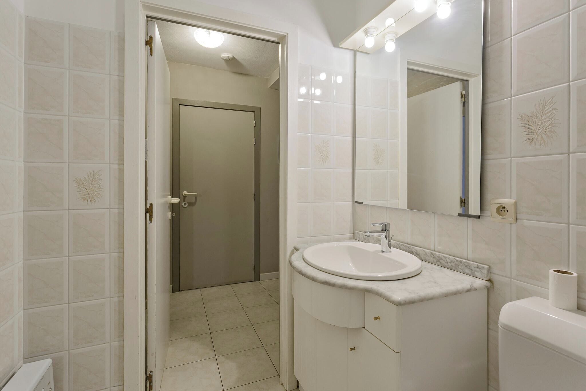 Un baño con lavamanos blanco, espejo y retrete.