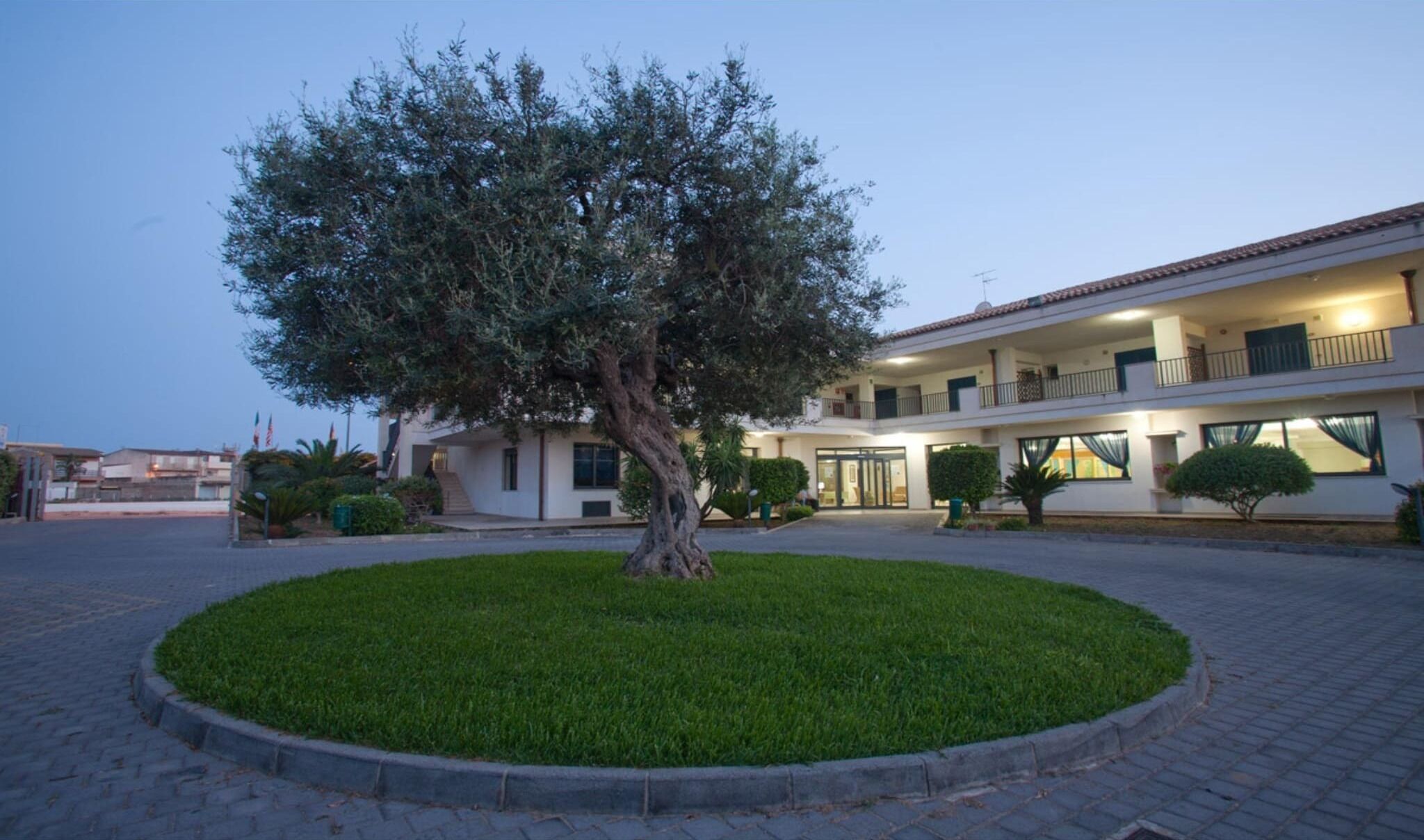 Un edificio con un cortile centrale, un albero grande e un prato curato.