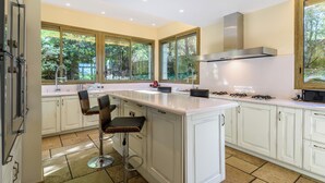 A modern kitchen with white cabinets, a large island with bar stools, and large windows offering views of greenery. - Exceptional villa between sea and mountains in a private estate in Saint Jean de Luz (Saint-Jean-de-Luz)