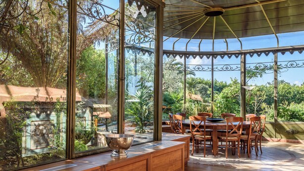 A conservatory with a wooden dining table and chairs, surrounded by large glass windows offering views of lush greenery. - Exceptional villa between sea and mountains in a private estate in Saint Jean de Luz (Saint-Jean-de-Luz)