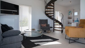 En moderne stue med et glasbord, en grå sofa, en gul lænestol, en spiraltrappe og et hvidt reolsystem.