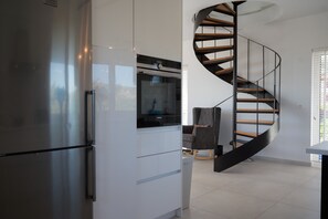 Enjoy a modern kitchen with refrigerator and sleek cabinetry, adjacent to a dining area with a chair and table.