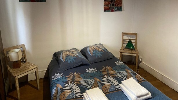 Ein Schlafzimmer mit einem Bett, zwei Kissen, einem Nachttisch, einer Lampe und zwei an der Wand befestigten Bildern.