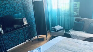 Habitación de hotel con dos camas, un televisor sobre un soporte, un escritorio y una ventana con cortinas.