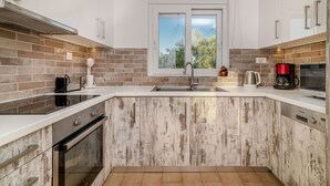 Een moderne keuken met witte kastjes, een backsplash van baksteen, een raam en een RVS spoelbak.
