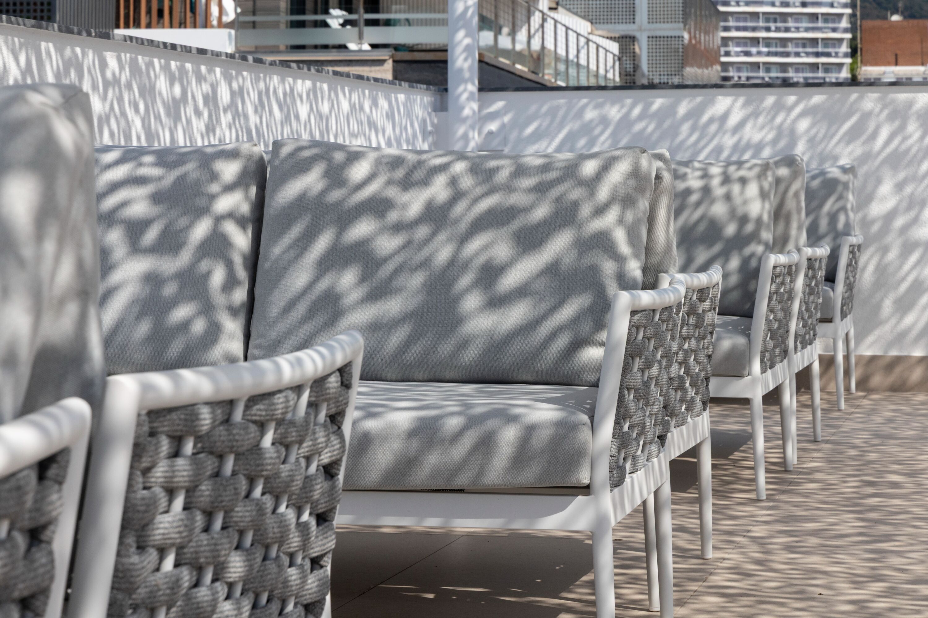 A row of white wicker chairs with grey cushions on a tiled patio.
