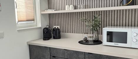 Una cocina moderna con encimera gris, microondas integrado y ventana con persianas.