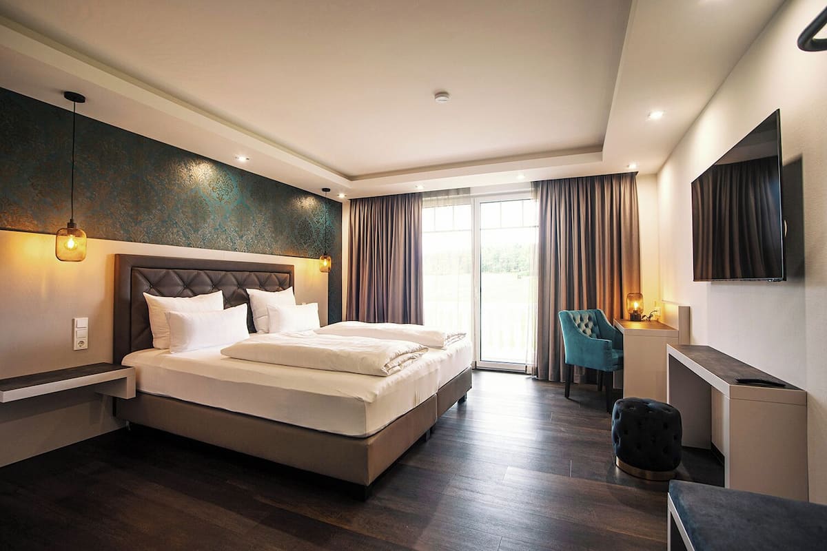 A modern hotel room with a large bed, a desk, a chair, and a TV.