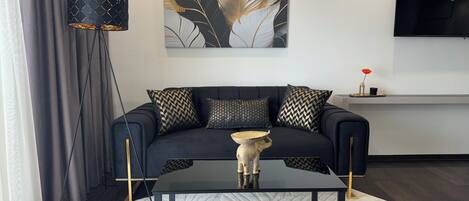 Una sala de estar moderna con un sofá negro, cojines estampados, una mesita de centro y un jarrón decorativo.
