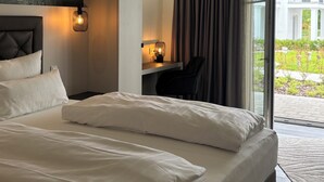 Hotelkamer met een groot bed, een bureau en een stoel. Er is een raam met gordijnen en uitzicht op buiten.