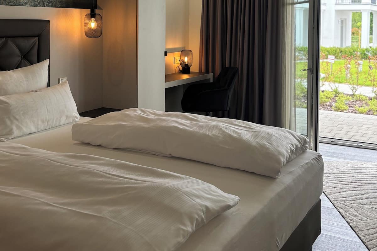 A hotel room with a large bed, a desk, and a chair. There is a window with curtains and a view of the outside.