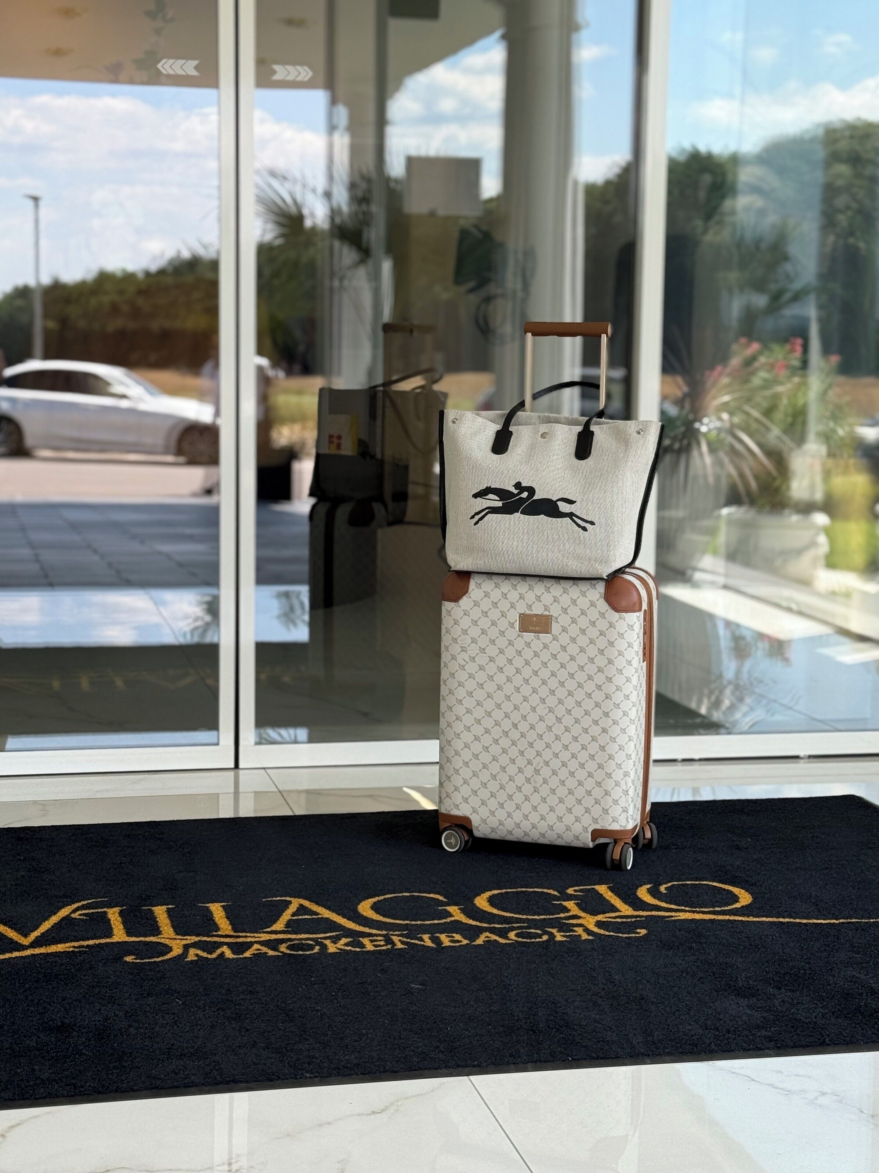A luggage cart with a patterned suitcase and a tote bag in front of a hotel entrance.