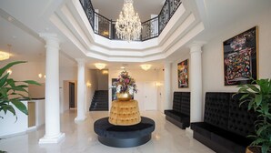 Een ruime lobby met een ronde centrale tafel, zwarte banken, een trap en een kroonluchter.