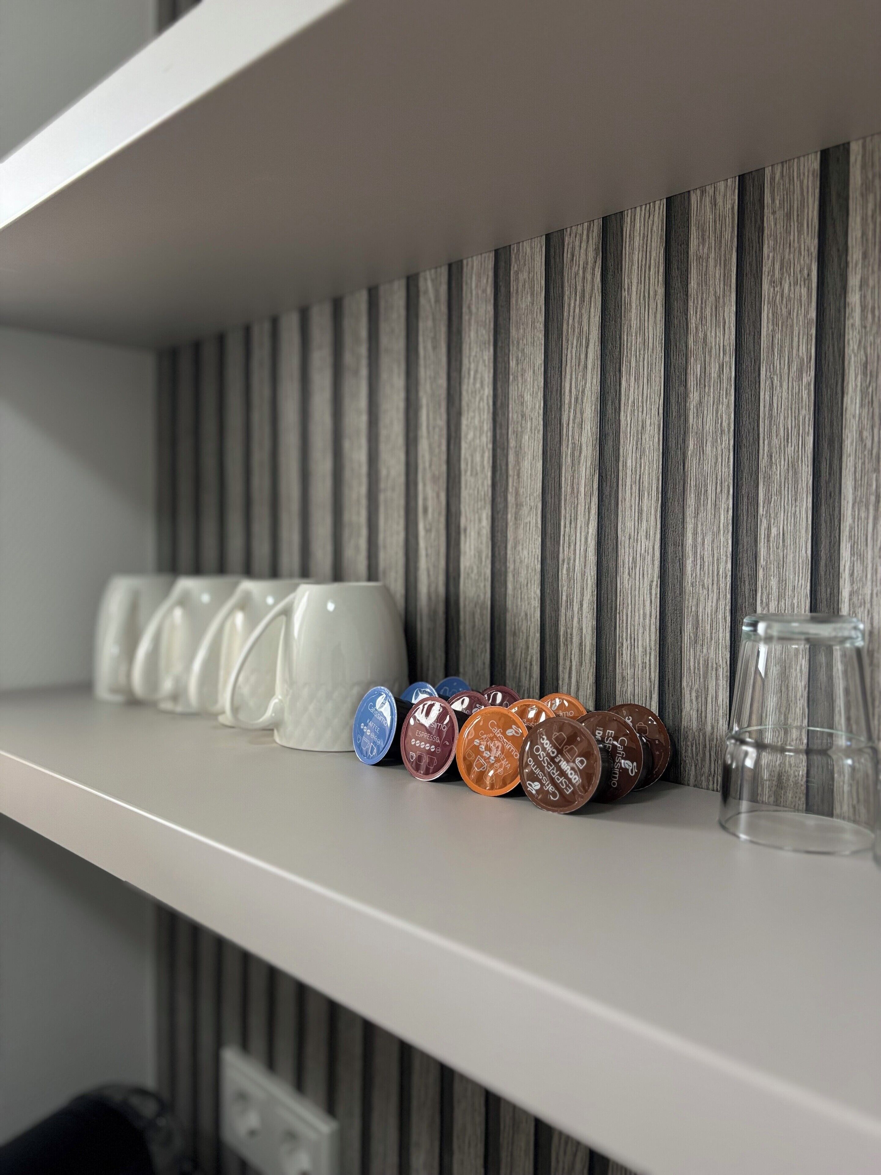 A shelf with coffee capsules and a glass.