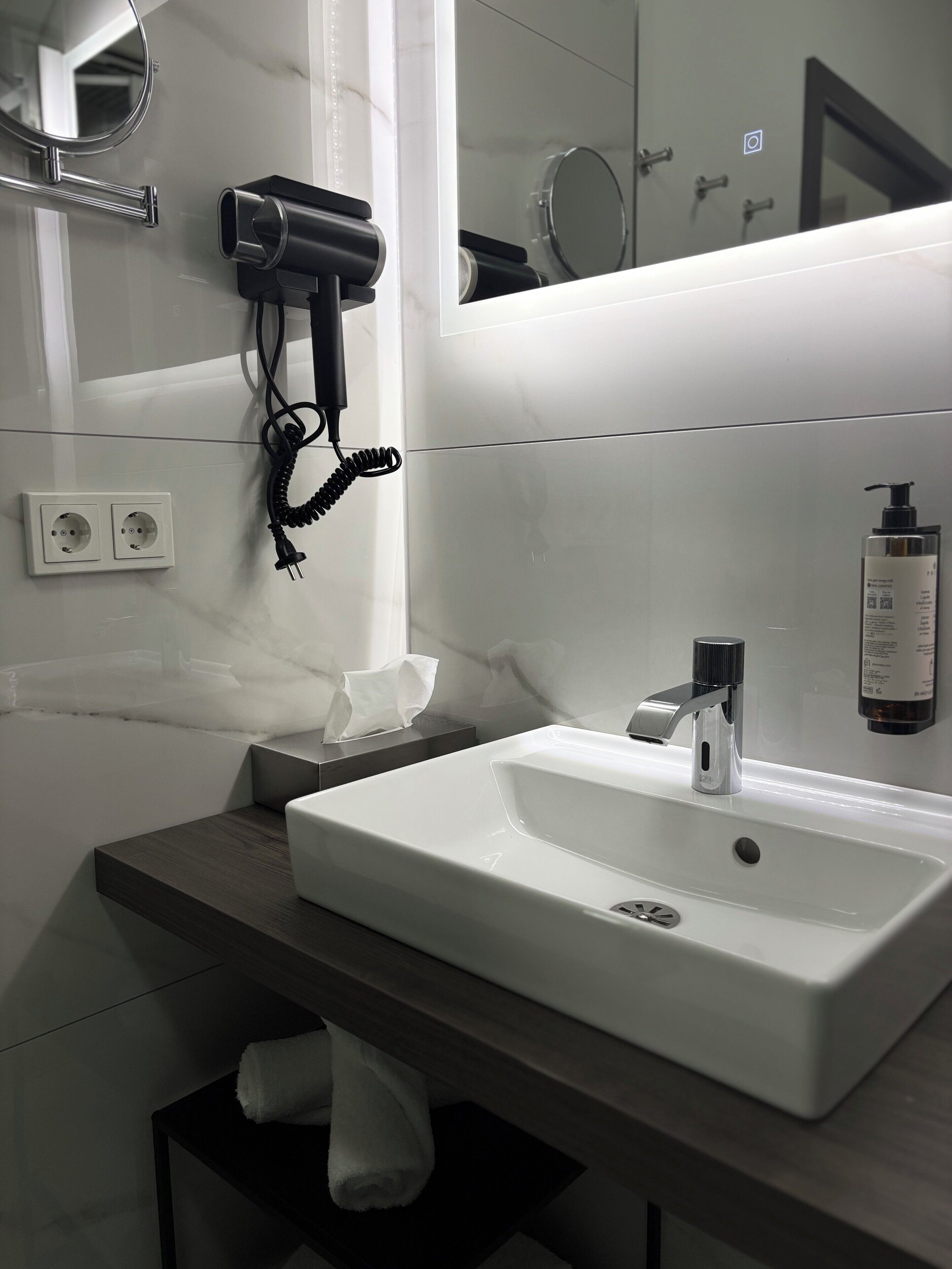 A modern bathroom with a white sink, a towel rack, a hairdryer, and a mirror.