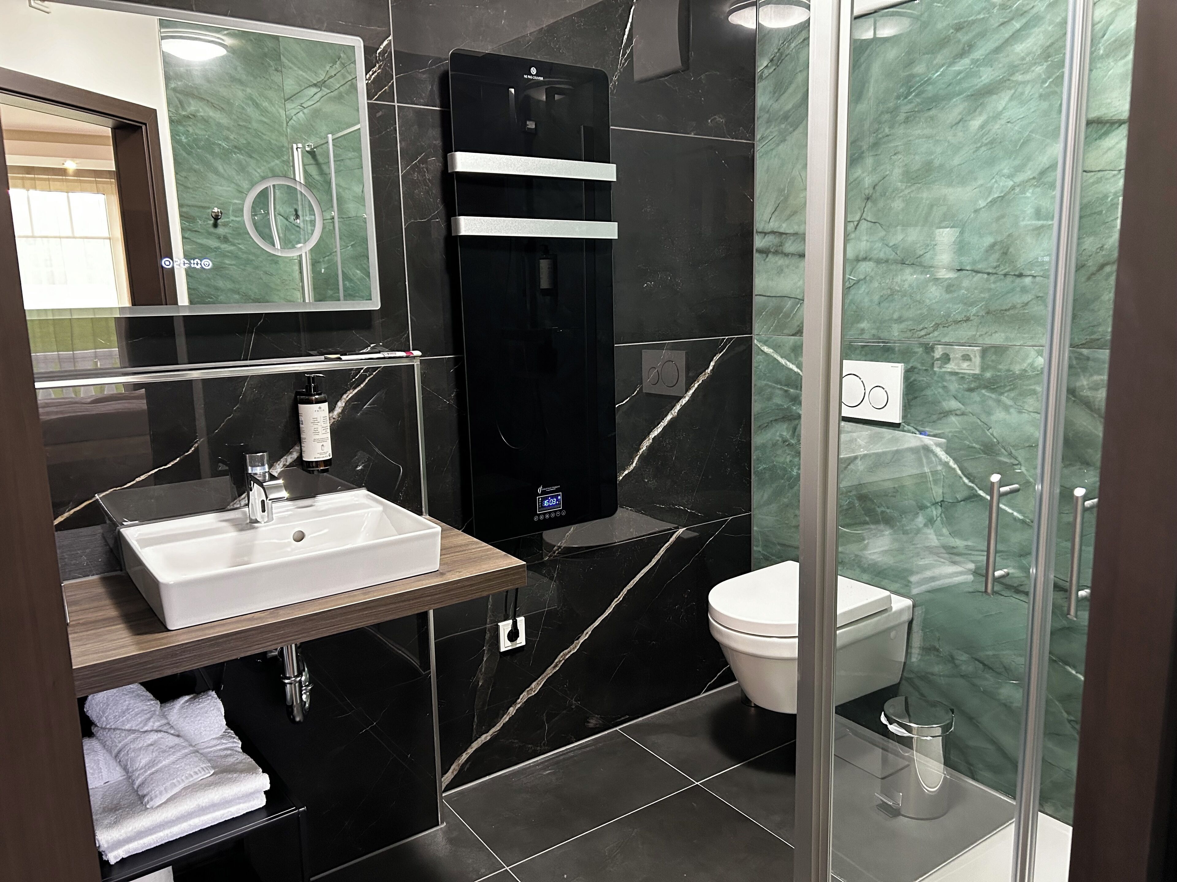 A modern bathroom with a black marble sink, a mirror, a black heater, a toilet, and a glass shower enclosure.