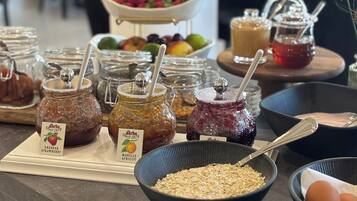 Una mesa de buffet con diversos alimentos, incluyendo frascos de mermelada, tazones de frutas y un bol de avena.