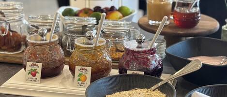 A buffet table with various food items including jars of jams, bowls of fruits, and a bowl of oats.